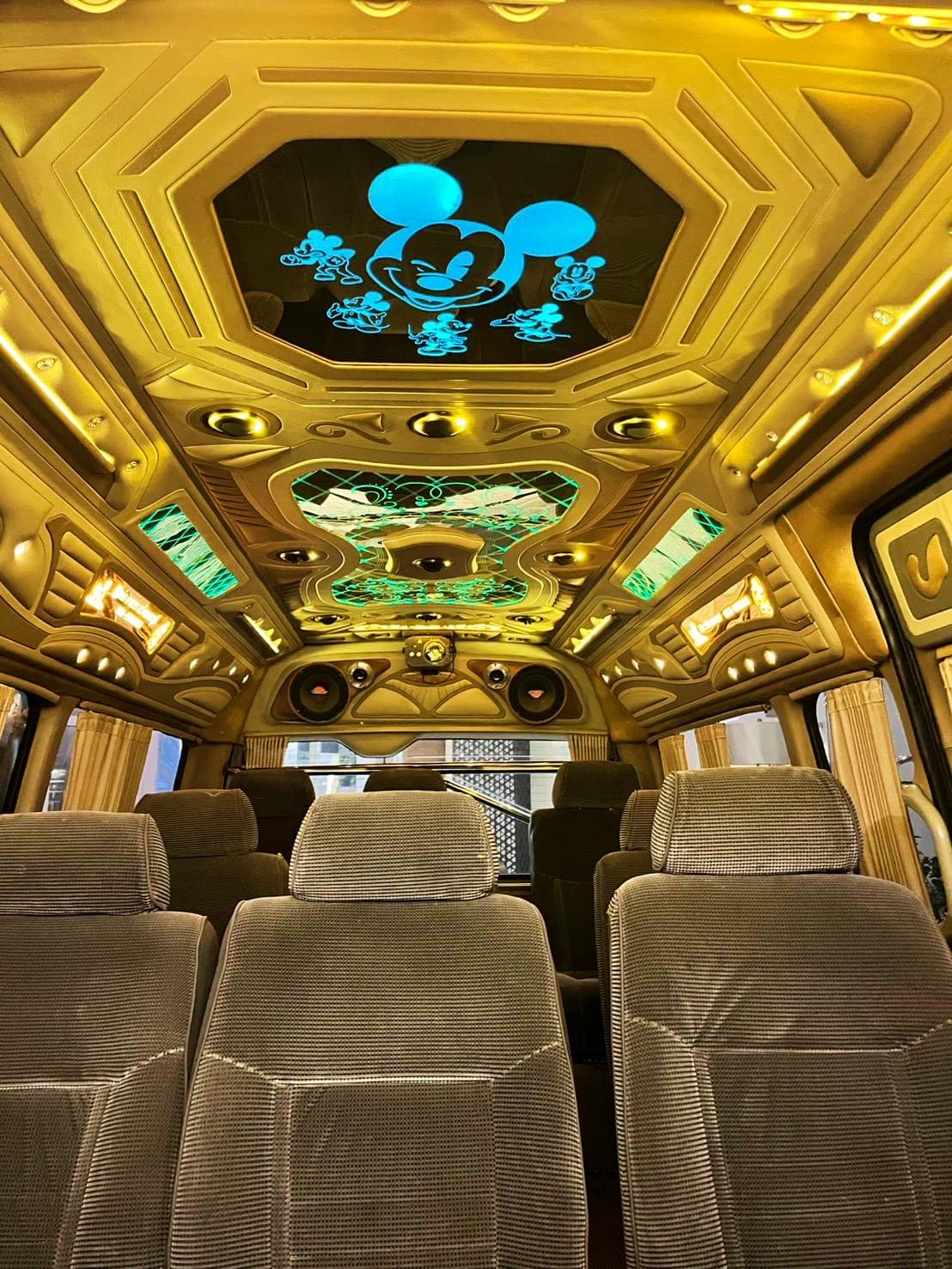 Hua Hin to Pattaya Hotel Transfers Luxury tour bus interior with gold ceiling panels featuring Mickey Mouse design and character graphics, beige seats, and deco